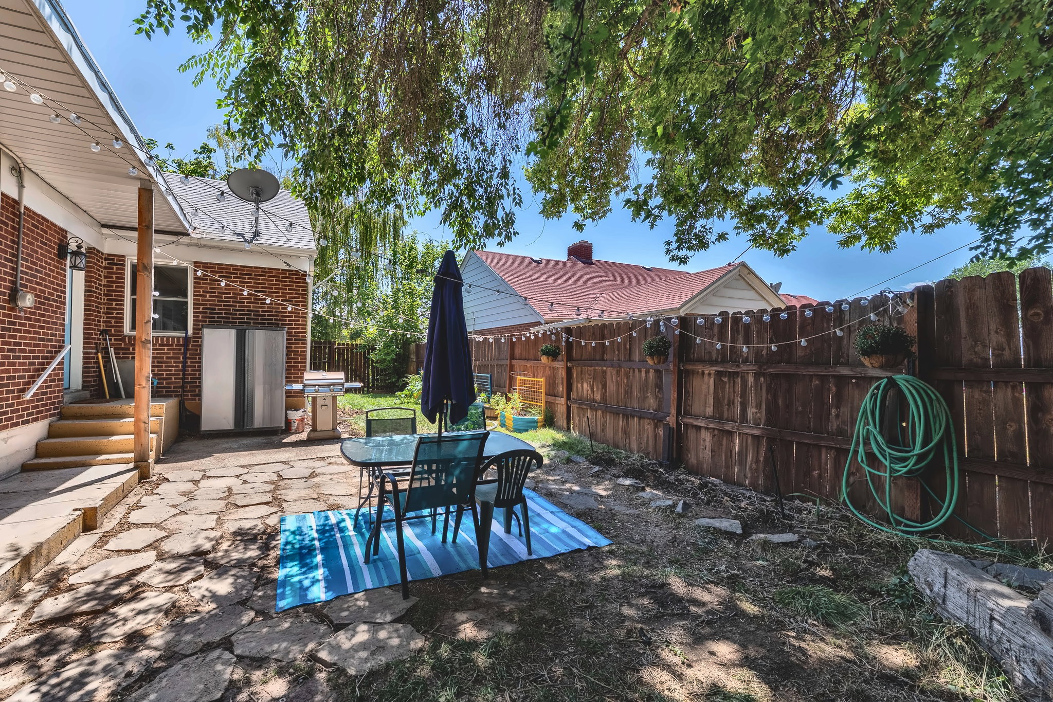 Brick exterior with a covered patio, flagstone patio, wood privacy fence, and mature trees providing shade