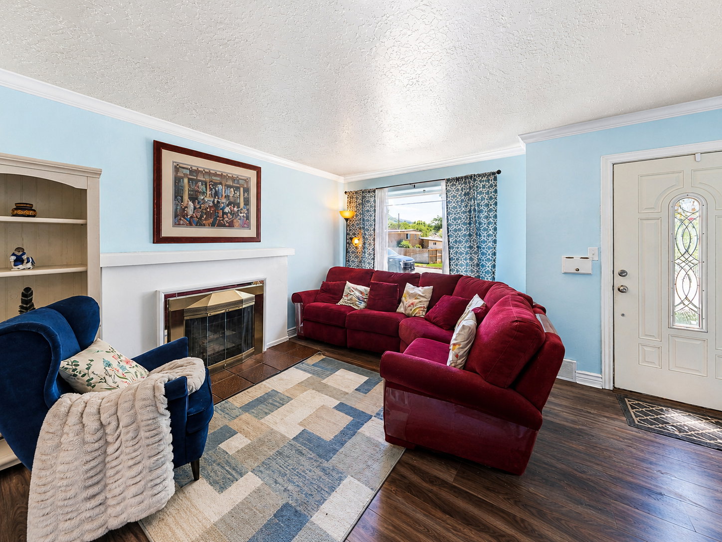 Living area featuring a fireplace with a brass firebox, built-in shelving, wood-finish flooring, a decorative entry door with frosted glass accents, and crown molding