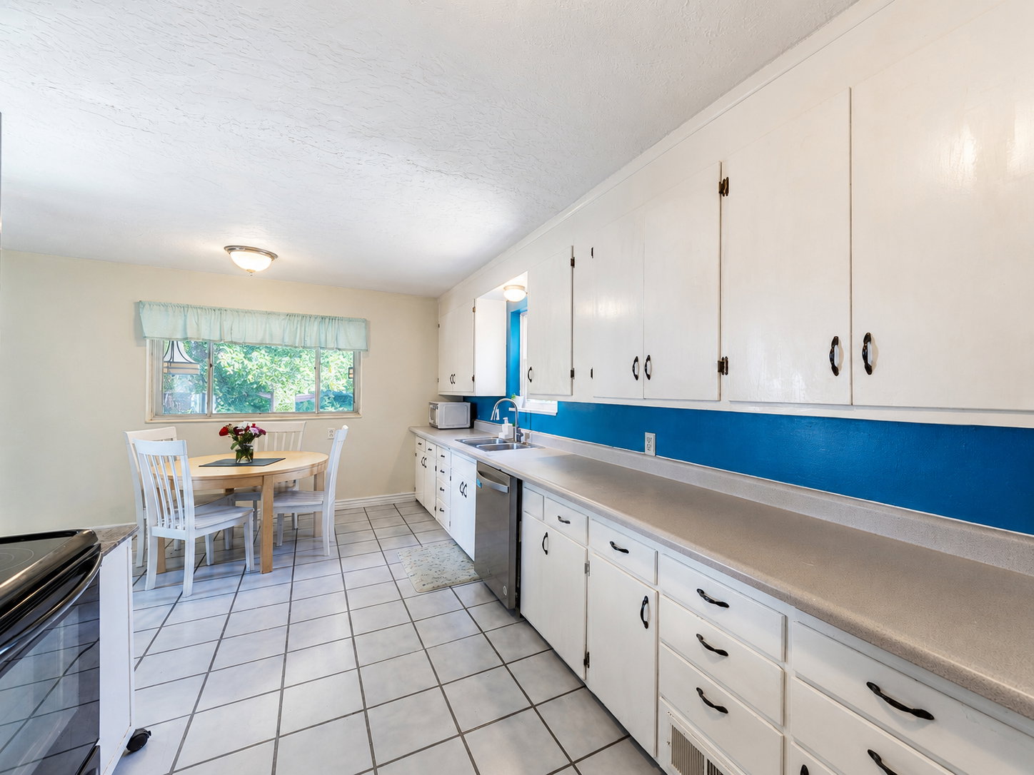 Kitchen featuring white cabinetry, light-toned countertops, stainless steel dishwasher, tile flooring, and a bright window