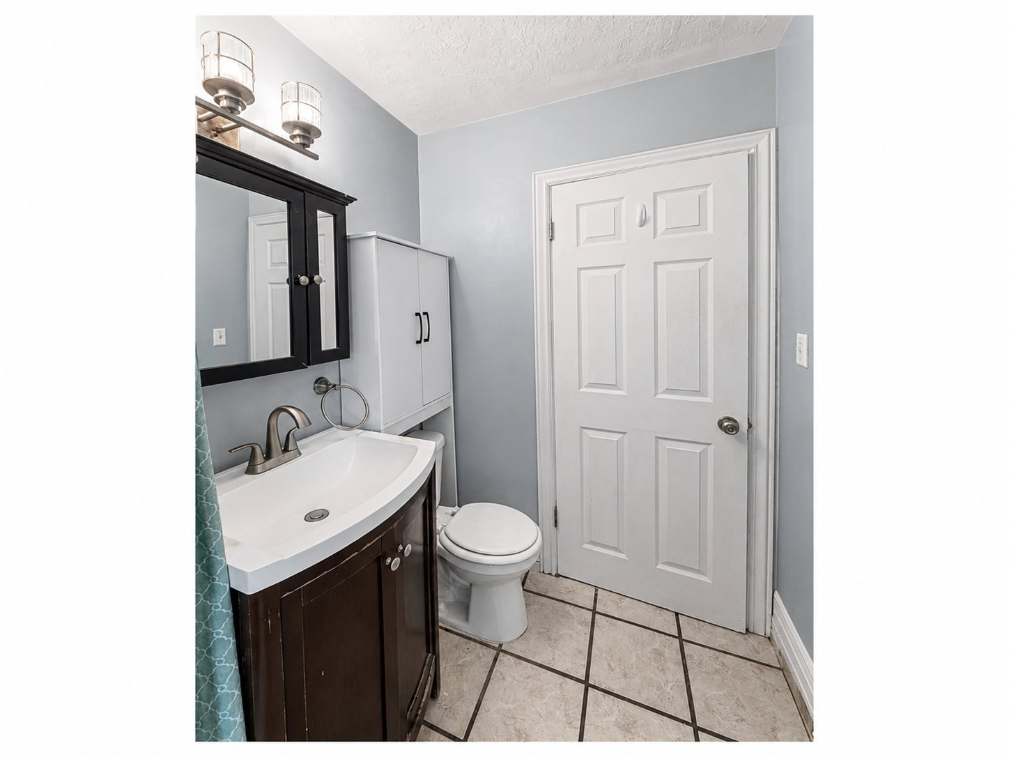 Bathroom featuring a dark wood vanity with white sink, white medicine cabinet, and a white six-panel door