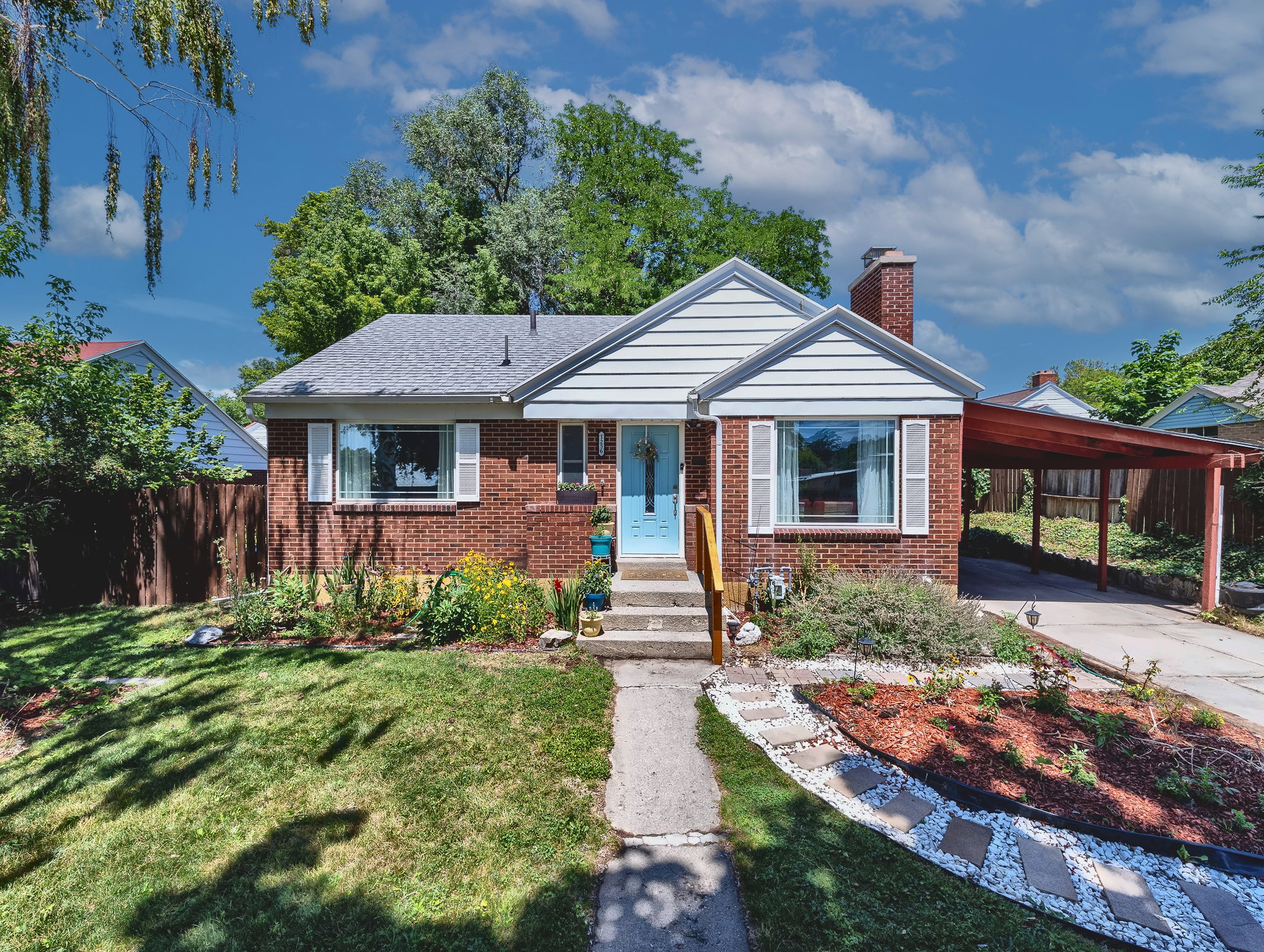 Brick facade residence featuring a light blue entry door, white shutters, and a covered carport