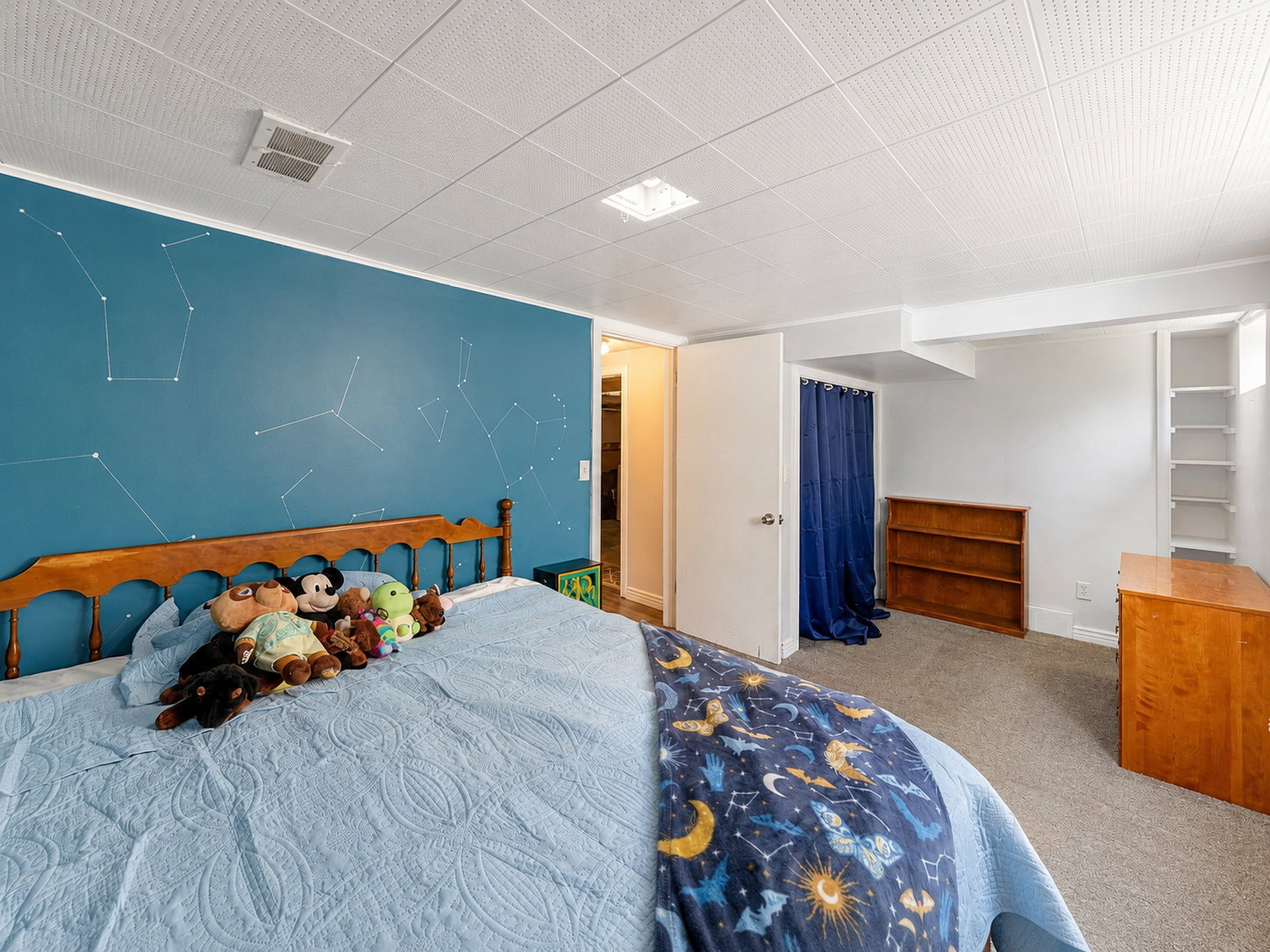 Carpeted bedroom featuring a patterned accent wall, white drop ceiling with recessed lighting, and a built-in shelving unit